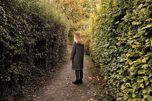 Young woman walks in the labyrinth of the autumn park. Outdoor adventure. Travel and Healthy lifestyle
