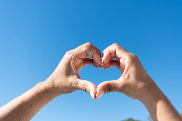 istock woman's hands showing heart sign on blue sky background 1460889995