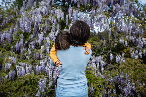 Rear view of Mother and a child hugging each other against flower backdrop