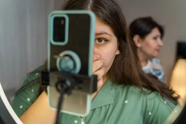 Photo of portrait of teenage girl filming videos at home and dancing to camera set on ring light, young blogger concept, copy space