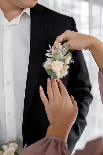 Bride corrects groom boutonniere on jacket at their wedding close-up details