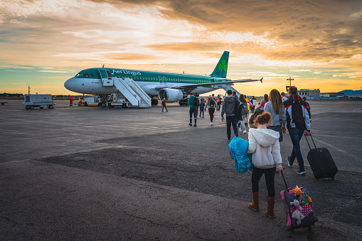 Perpignan, France, Jan People going to airplane parked on airport runway. Tourists boarding Aer Lingus Boeing airplane in morning, at dramatic sunrise