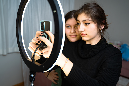 portrait of teenage girl filming videos at home and dancing to camera set on ring light, young blogger concept, copy space