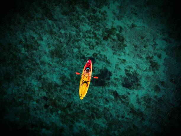 Aeriel panorama of young female person woman girl in red yellow kayak floating on clear blue ocean water Mallorca Spain stock photo