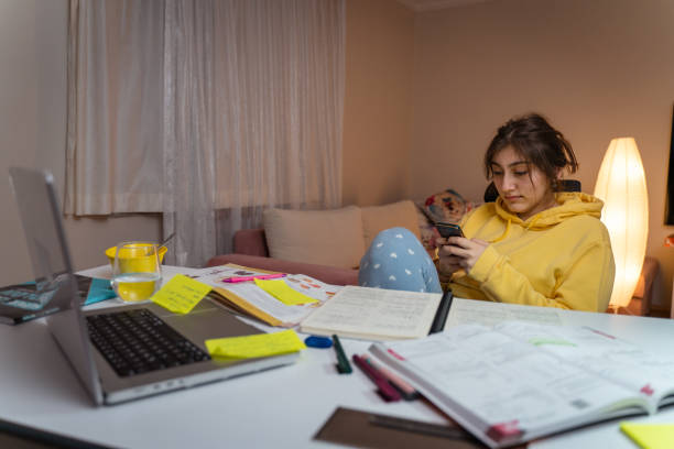 Girl is Working on Homework for School. Young Female Reading Research Articles About Her Hobby. Education Concept Bored girl scrolling apps on phone, distracted from homework, procrastination wasting time stock pictures, royalty-free photos & images