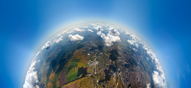 Aerial view from high altitude of little planet with distant city covered with puffy cumulus clouds flying by before rainstorm. Airplane point of view of landscape in cloudy weather.