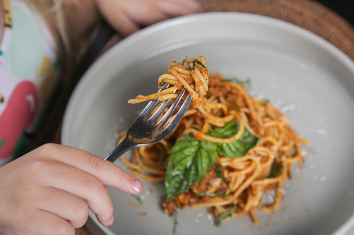 Little girl eating a portion of spaghetti bolognese at the restaurant