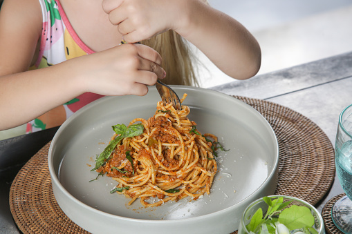 Little girl eating a portion of spaghetti bolognese at the restaurant