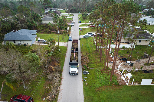 Aerial view of Hurricane Ian special aftermath recovery dump truck picking up vegetation debris from Florida suburban streets. Dealing with consequences of natural disaster.