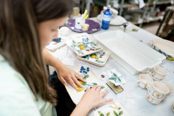 Female worker applying decals on plates while working at a table in a ceramics manufacturing workshop