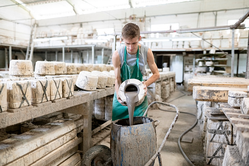 Young male potter working with ceramics pouring clay from mold in can at a ceramic factory