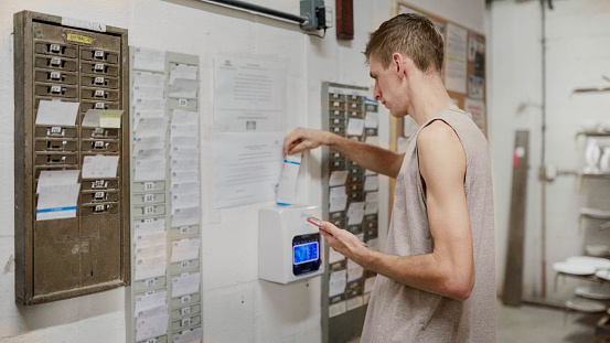 Young male worker arriving at work and punching his time card in a clock before starting his factory shift