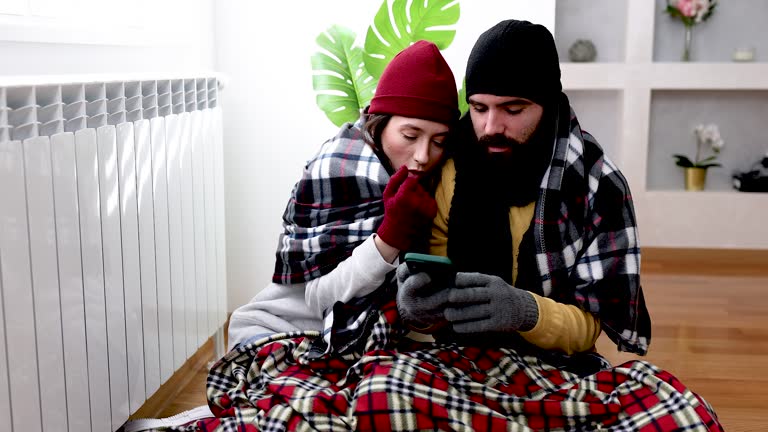 A young couple is suffering from a cold temperature during an energetic crisis and trying to warm up near the radiator.