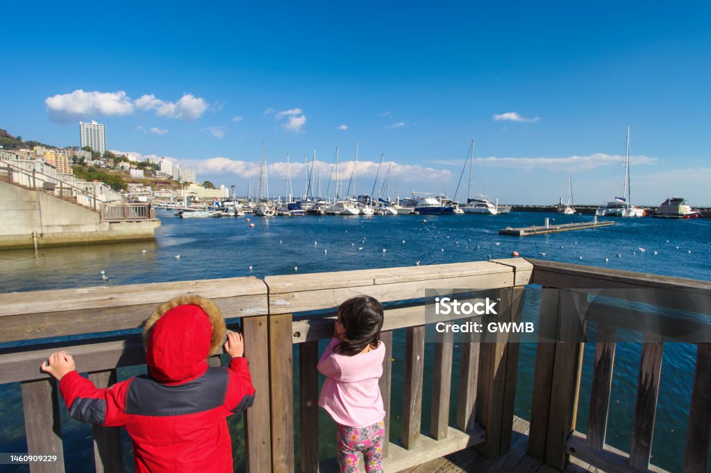 Two children at Atami Promenade or Rainbow Deck in Atami City, Shizuoka Prefecture, Japan. Two children at Atami Promenade or Rainbow Deck in Atami City, Shizuoka Prefecture, Japan with moored sailing boats at the marina on the right side. Atami is a getaway for people living in the Tokyo area. 4-5 Years Stock Photo