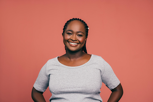 A portrait of a smiling African-American female standing against pink background. (studio shot, copy space)