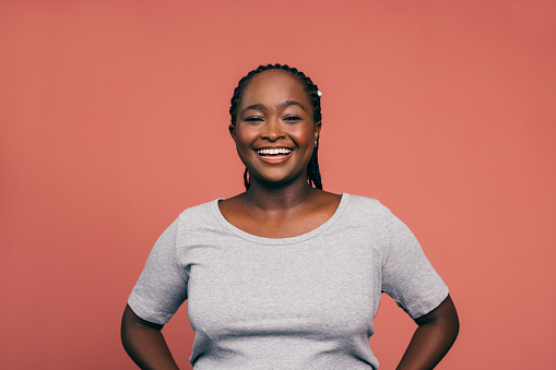 A portrait of a smiling African-American female  looking excited while standing against pink background. (studio shot, copy space)