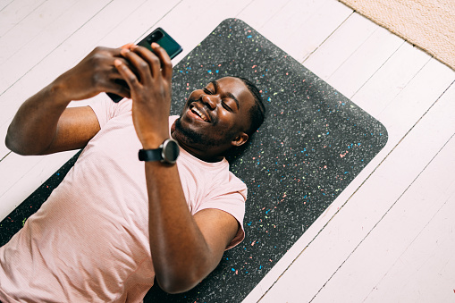 A from above view of a smiling African-American athlete using his smartphone after doing his daily workout.