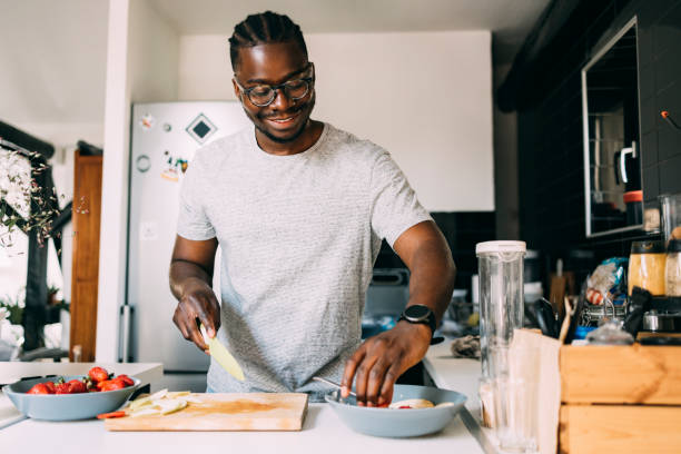 ein glücklicher mann mit gläsern, der gesundes frühstück zubereitet, während er in der küche steht - strawberry fruit single object food stock-fotos und bilder