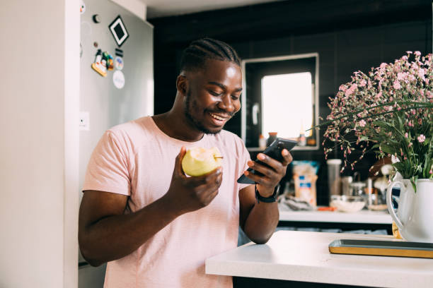 A Happy Man Watching Something On His Mobile Phone While Eating An Apple
