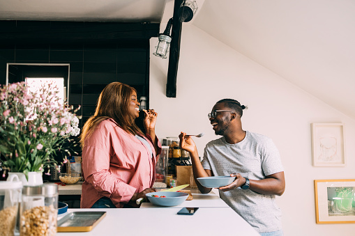 A side view of a smiling African-American couple standing in the kitchen and having a healthy meal together.