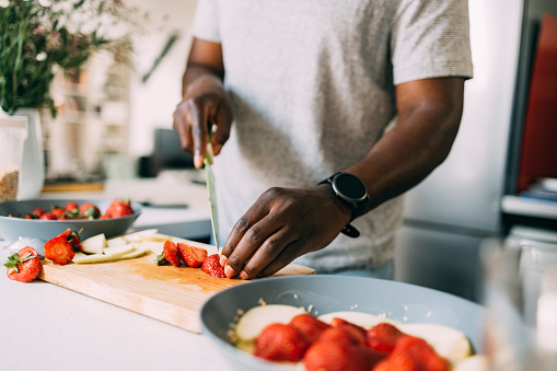 An anonymous African-American male cutting strawberries while making a healthy meal.