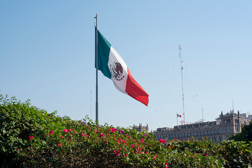 Mexican flag waving with blue sky and the government building of Mexico City in Mexico City