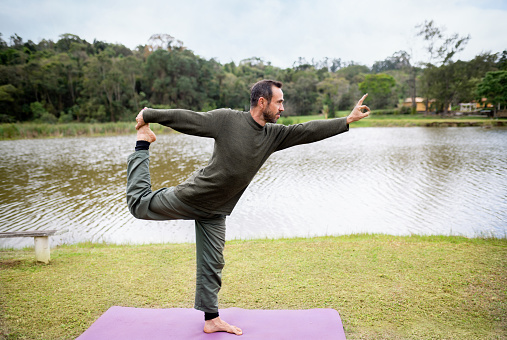 Fit man doing the standing bow pose during a lone yoga session outside by a lake