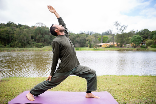 Fit man practicing the crescent lunge pose during a lone yoga session outside by a lake