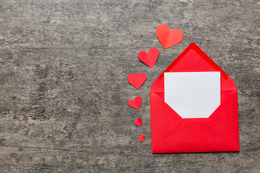 Red paper envelope with empty white card and heart on colored background. top view valentines day concept.