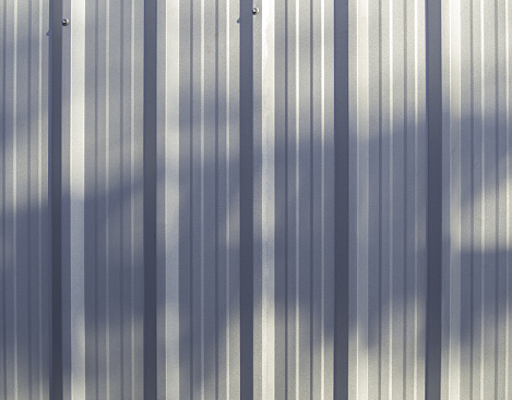 The wall or background of the metal sheet. The background pattern is a vertical pattern and reflected light from the sun and tree shadows.