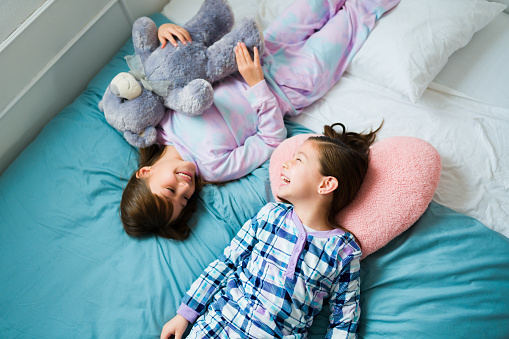 Cute kids and best friends in pajamas and a teddy bear laughing having a lot of fun during a sleepover