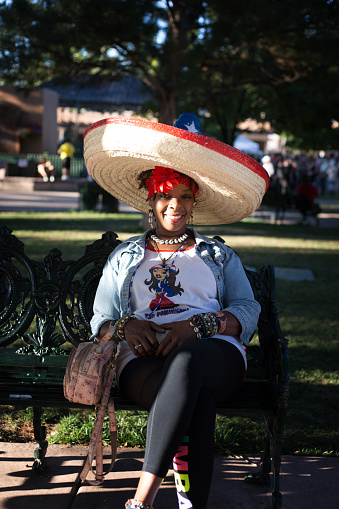 Santa Fe, NM: A tourist with a sombrero sits on a bench on the historic Santa Fe Plaza looking at the camera.