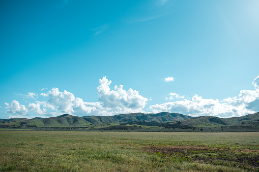 Outdoor shot of a sunny landscape with clear blue sky. Green grass and beautiful clouds in this environment. Mountain scenery.