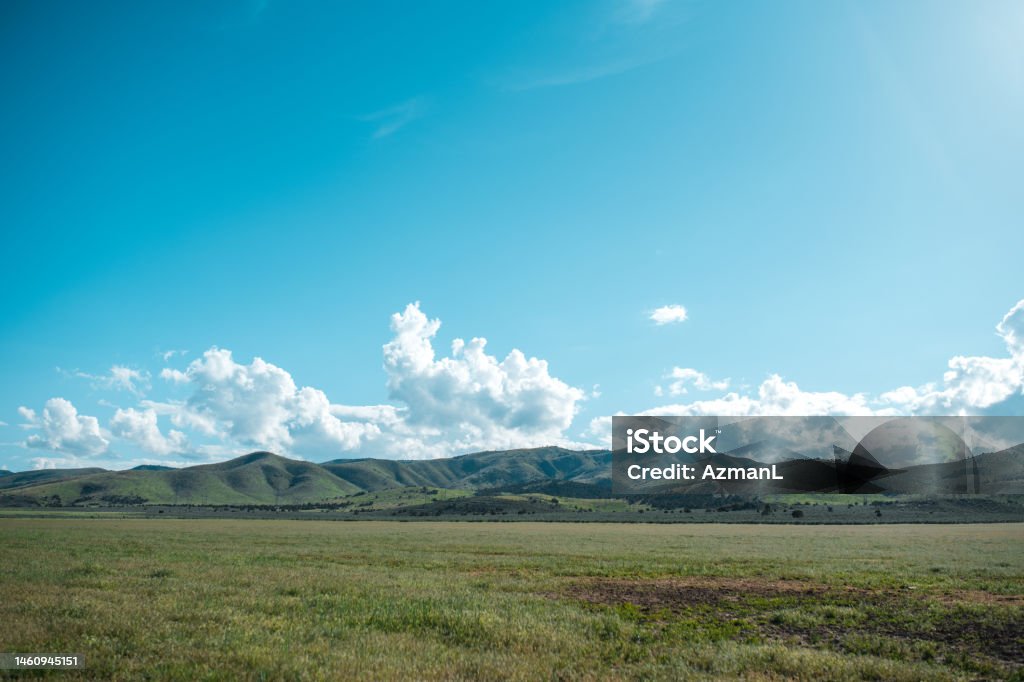 Sunny Landscape with Clear Blue Sky Outdoor shot of a sunny landscape with clear blue sky. Green grass and beautiful clouds in this environment. Mountain scenery. Mountain Range Stock Photo