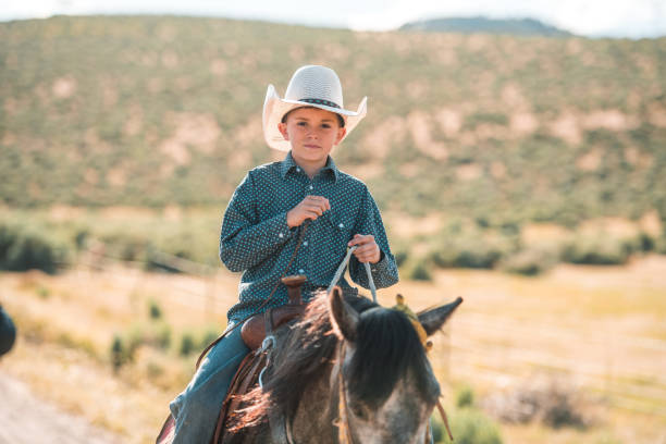 istock Happy Young Cowboy Kid Riding a Horse Using a White Hat 1460945165