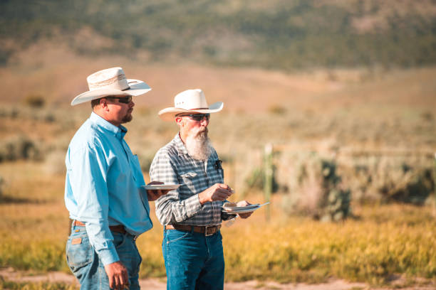 Outdoor shot of two male adults talking and eating next to each other. They are part of a rodeo and wears the same cowboy hats and similar shirts.