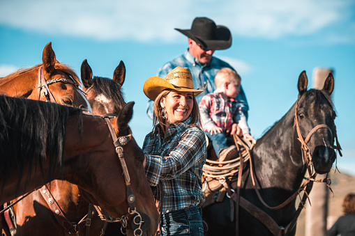 Outdoor shot on a sunny day where a smiling family has a good time at the ranch. They are riding horses and petting them.