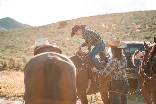 Calm shot of brave kid mounting a horse for the first time. His mother is helping him out as he secures his legs around.