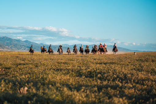 Big group of cowboys and cowgirls having a blast together. They are horseback riding in the open field, their horses are running fast.