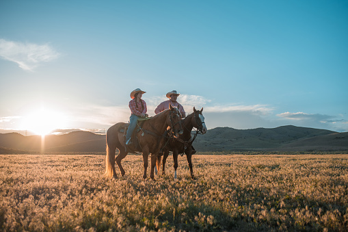 Lovely mid adult couple relaxing while riding horses. They are breathing the fresh air from the countryside. They wear matching cowboy hats.