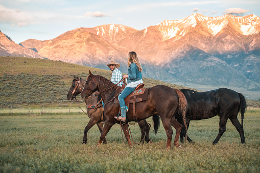 Colorful afternoon date. Full length shot of good looking couple horseback riding together. The man is wearing a cowboy hat and the are both wearing comfortable clothing.