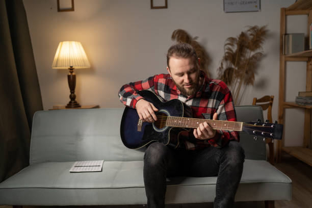 istock Handsome bearded man playing guitar while sitting on sofa in living room in the evening. 1460953168