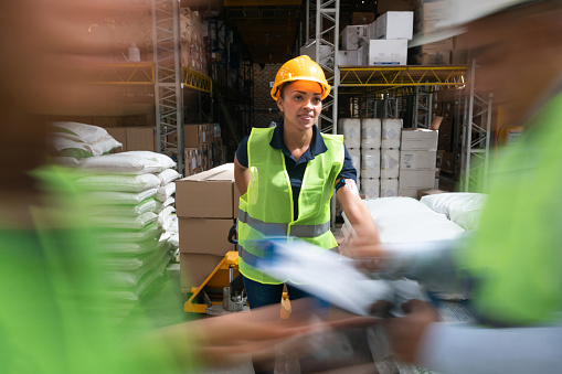 Happy Latin American woman working at a distribution warehouse moving boxes with a forklift - blurred motion concepts
