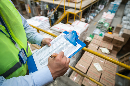 Close-up on an operator making an inventory at a distribution warehouse and writing on a clipboard