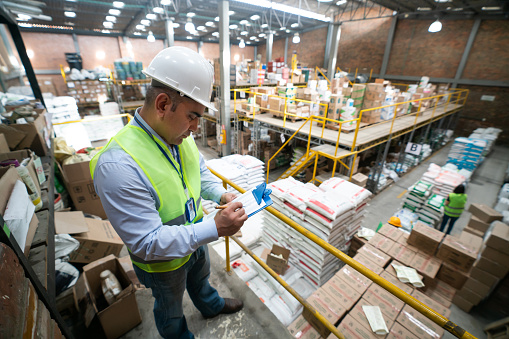 Latin American man working at a distribution warehouse and writing on his clipboard - people at work concepts