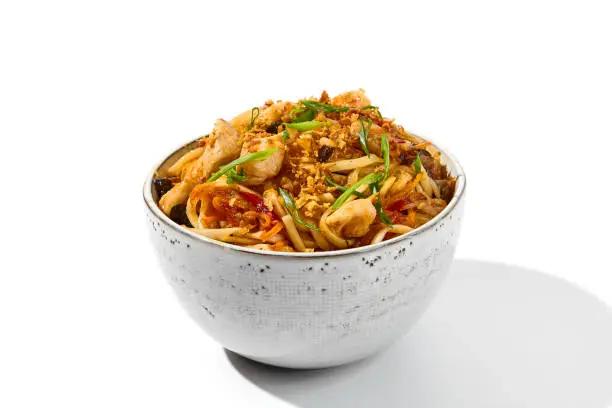 Asian fried noodles with chicken and vegetables isolated on white background. Chinese fried noodles with chicken meat and shiitake mushrooms in ceramic bowl. Stir-fry udon with vegetables and meat