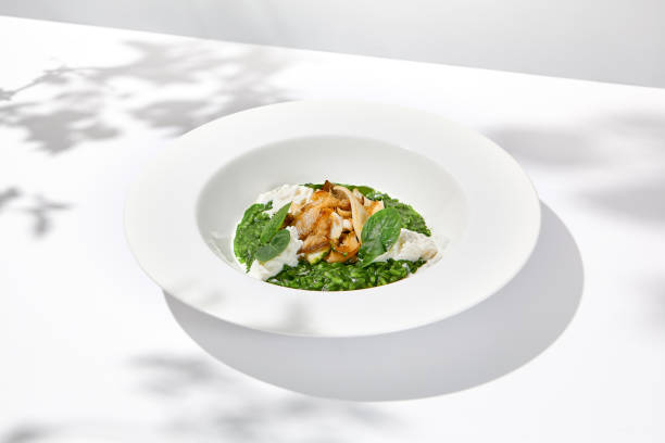 istock Green risotto with squid and stracciatella cheese on white plate. Creamy risotto with spinach, calamari and creamy cheese. Italian risotto with squid on light background with shadows of leaves 1460956189