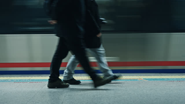 SLO MO Two people walk past the camera, while a subway train passes in the background