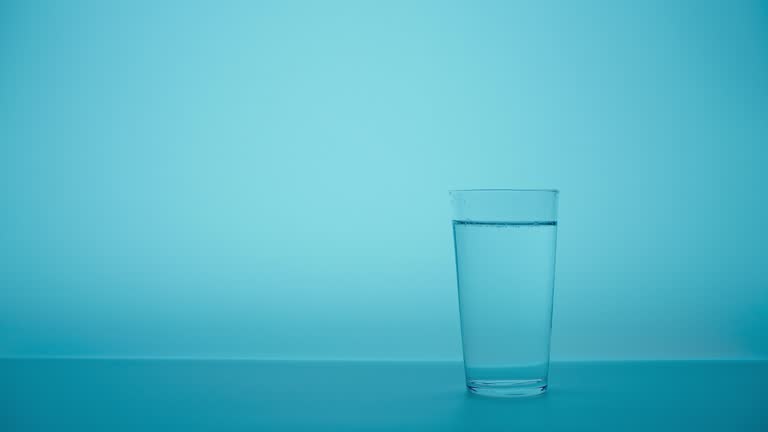 Pouring drink water to glass of water. Close up pouring fresh clean drinking water into glass, splashing in glass on light blue background.