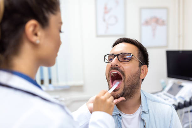 male patient opening his mouth for the doctor to look at his throat. female doctor examining sore throat of patient in clinic. otolaryngologist examines sore throat of patient. - doctor patient male tongue depressor imagens e fotografias de stock